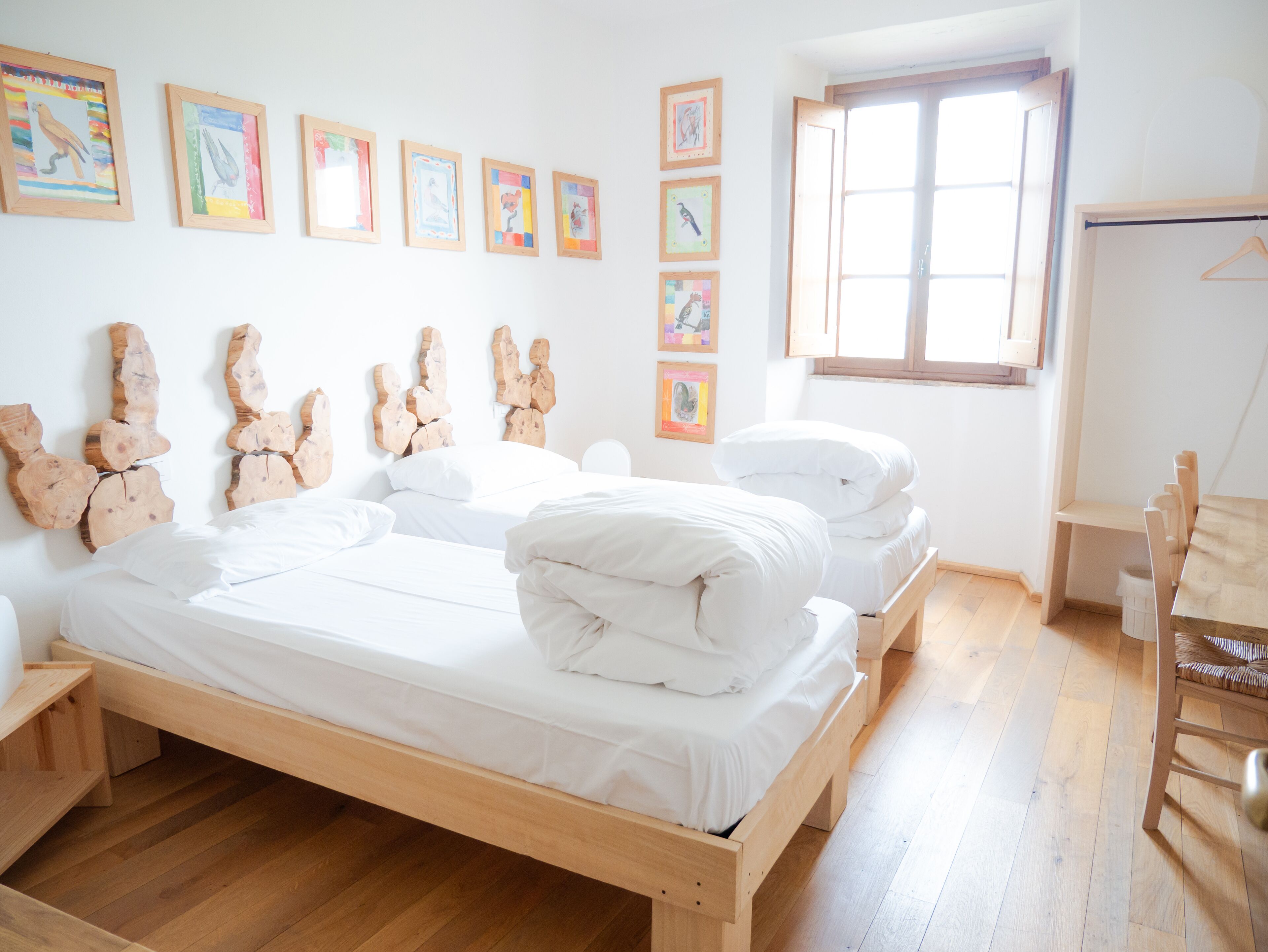 Un dormitorio con cama de madera, ropa de cama blanca y suelo de madera. Hay esculturas de madera y cuadros enmarcados en la pared.