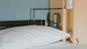 Ein Bett mit weißen Laken, einem Holz-Kopfteil, einer Wandlampe und einem Handtuch, das an einem Holzboden hängt.