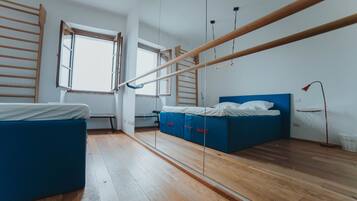 Una habitación con piso de madera, una cama con cabecera azul, un escritorio pequeño, una escalera y una ventana.