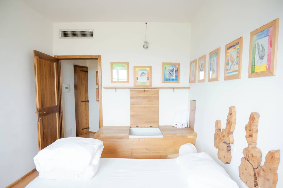 A bedroom with a wooden bed, a wooden desk, and a view of a room with a wooden door.