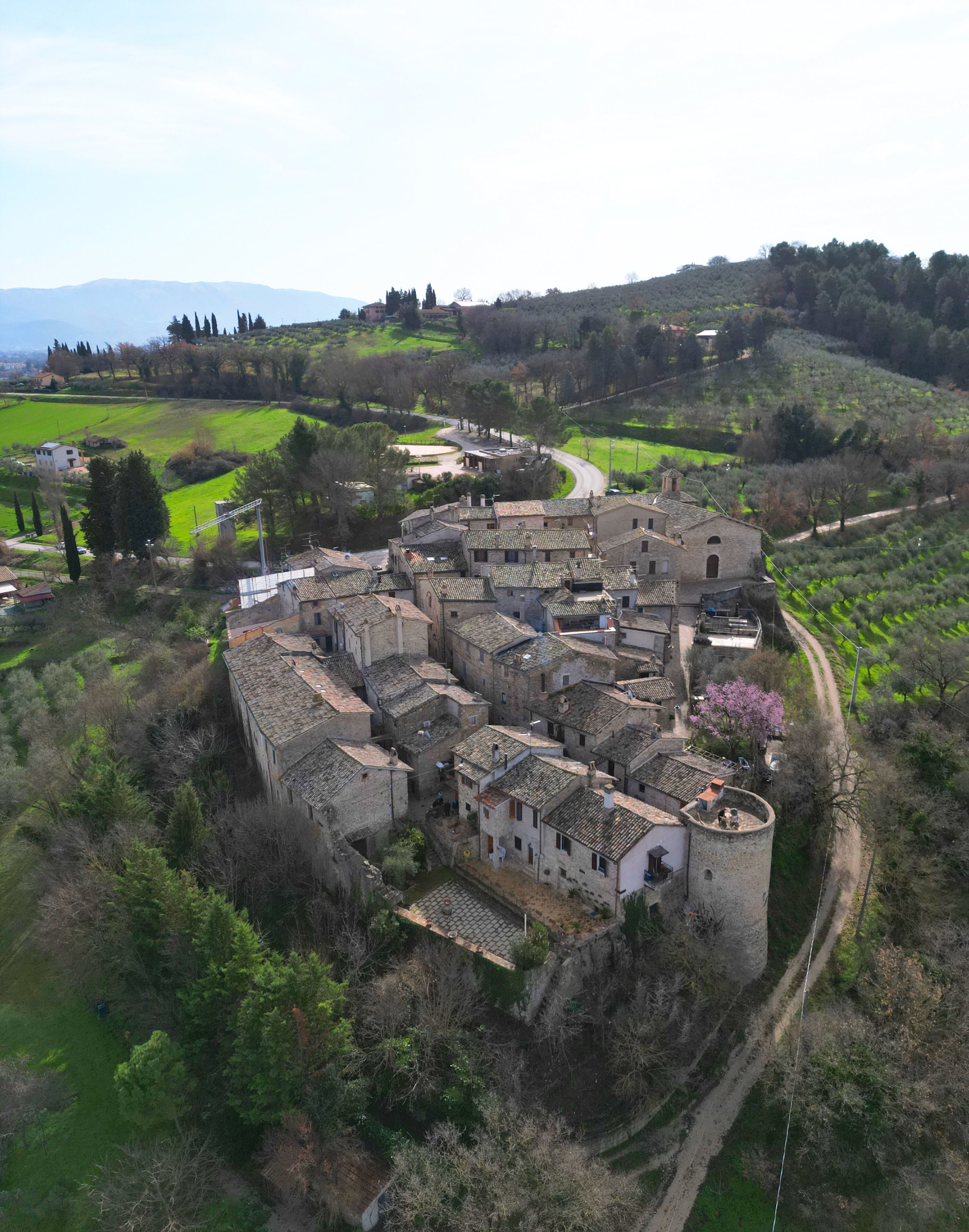 Vue aérienne d’un village historique, avec ses bâtiments en pierre, ses rues étroites et la verdure environnante.