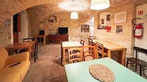 A rustic room with stone walls, a wooden dining table, chairs, a television, and a bookshelf. - Ostello Bello Assisi Bevagna (Bevagna)