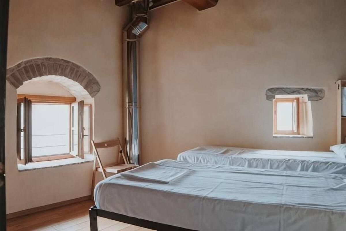 A bedroom with a bed, an arched window, a chimney, and a small window.