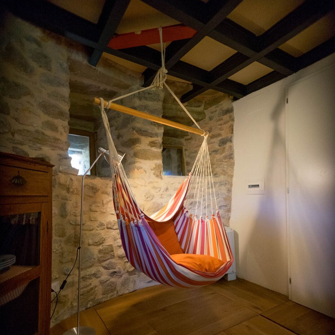 A room with a stone wall, a wooden floor, a hanging hammock, and a wooden cabinet.