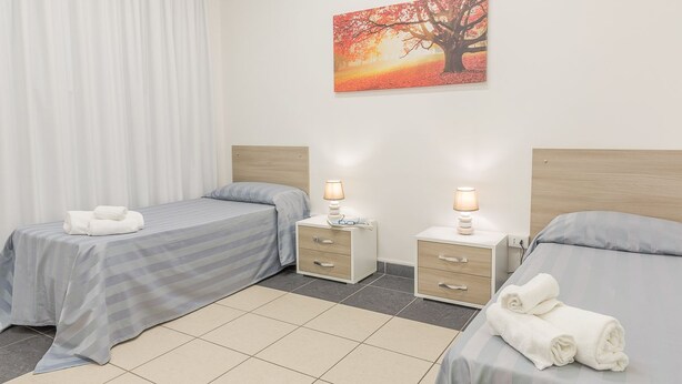A hotel room with two beds, a nightstand with a lamp, and a painting of a tree. - Casa per ferie Don Orione Palermo (Palermo)