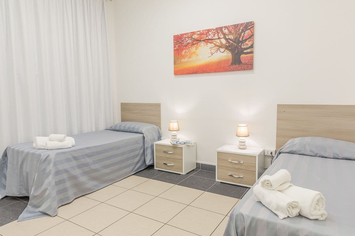 Una habitación de hotel con dos camas, una mesita de noche con lámpara y un cuadro de un árbol.