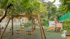 A playground with swings, slides, and climbing structures surrounded by trees and a fence. - Casa per ferie Don Orione Palermo (Palermo)