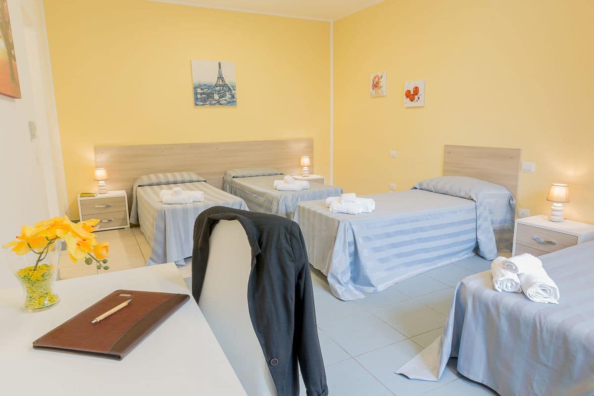 Habitación de hotel con dos camas individuales, un escritorio con silla, un florero con flores y obras de arte en las paredes.