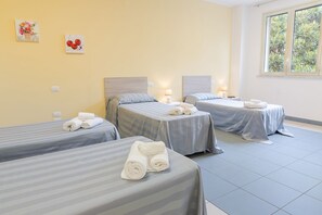 Habitación de hotel con dos camas individuales, cada una con una almohada y una toalla enrollada. Hay dos lámparas de pared en cada cama, y una ventana con vistas a zonas verdes.