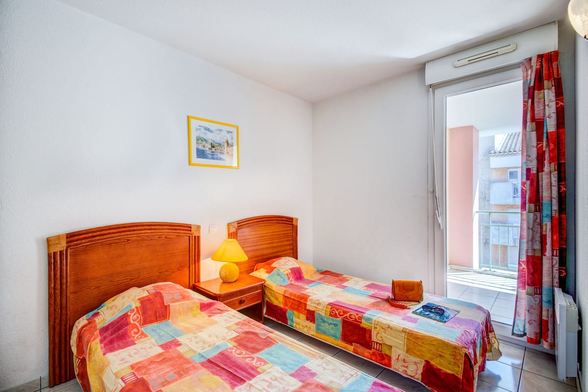 Un dormitorio con dos camas, una mesita de noche con lámpara, un cuadro enmarcado en la pared y vistas al balcón exterior.