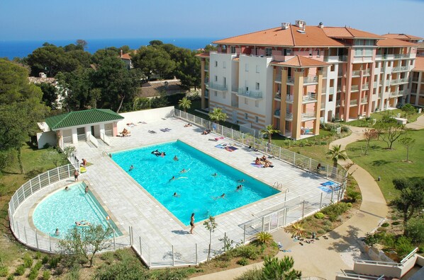 A hotel with a large pool area, multiple balconies, and a view of the sea. - Vacancéole - Les Calanques du Parc (Fréjus)