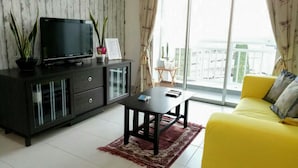 A modern living room with a flat-screen TV on a dark wooden cabinet, a yellow sofa, and a large window with a view of buildings.