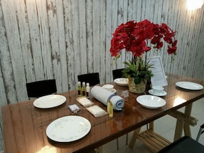 Una mesa de comedor con platos, una toalla enrollada, artículos de aseo y una planta en maceta.