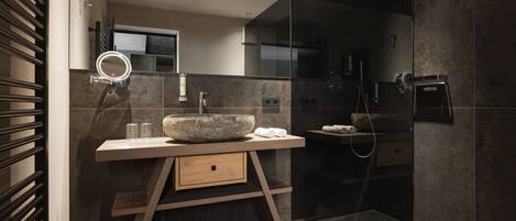 A modern bathroom with a large mirror, a stone sink, and a walk-in shower.