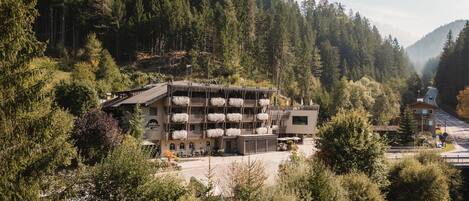 A modern building with a flat roof, surrounded by dense forest and hills.