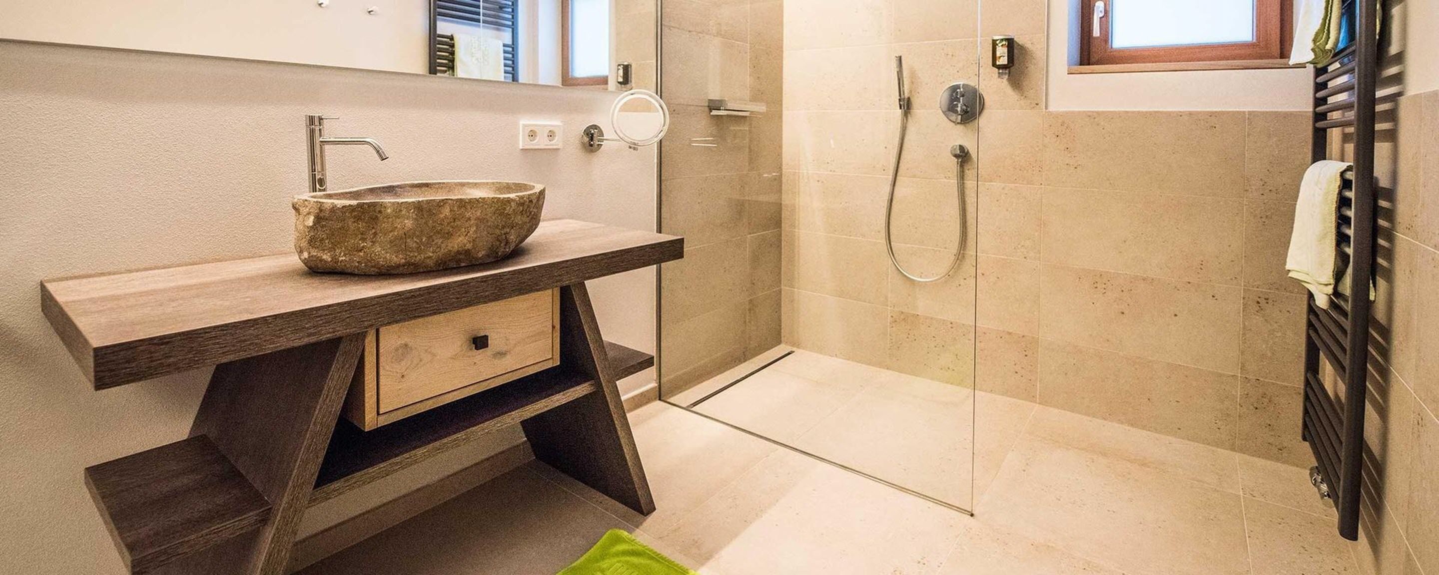 Une salle de bain avec un lavabo en pierre, un meuble-lavabo en bois, une cabine de douche en verre et un porte-serviettes.