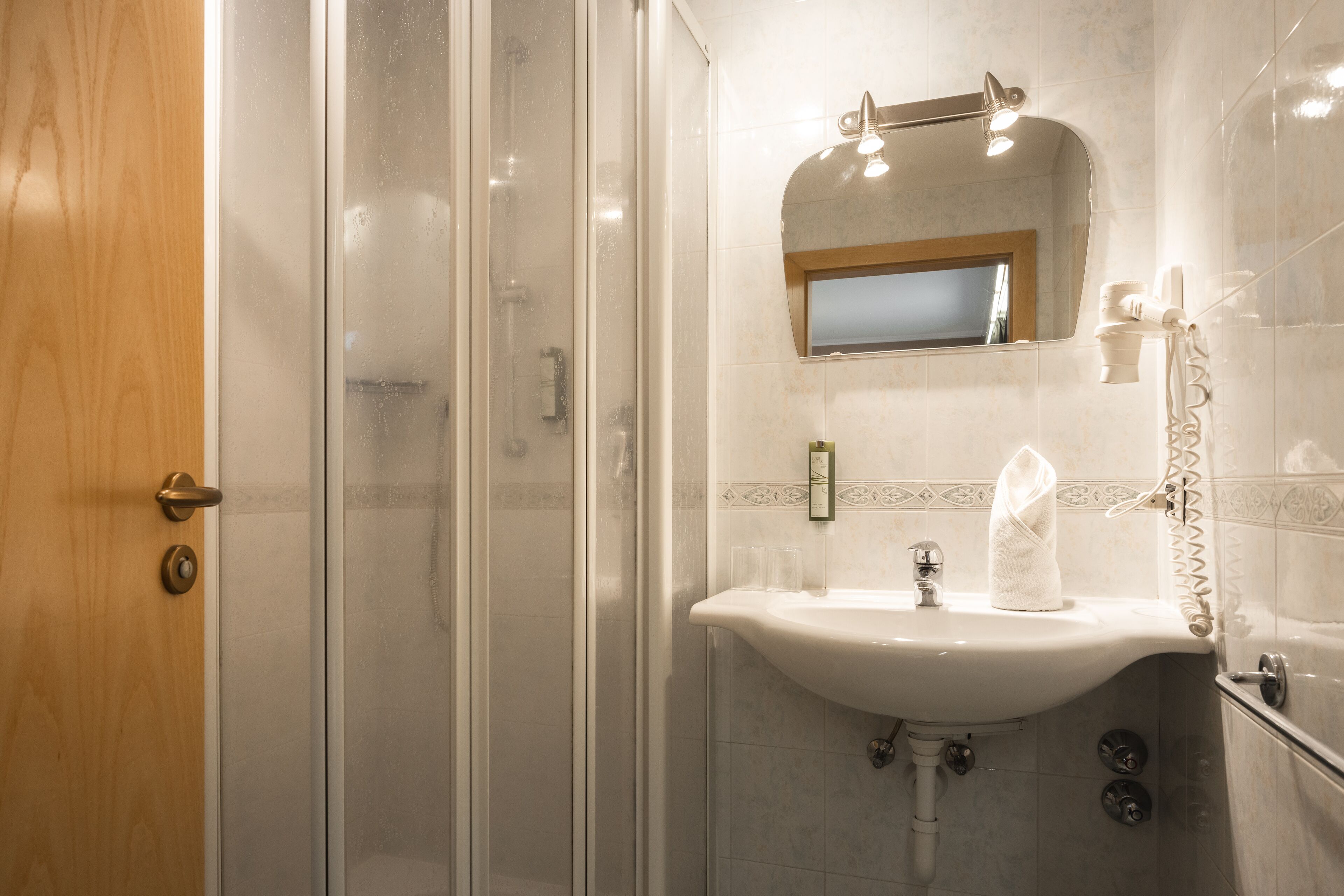 A bathroom with a glass shower enclosure, a sink with a mirror above it, and a towel hanging on the wall.