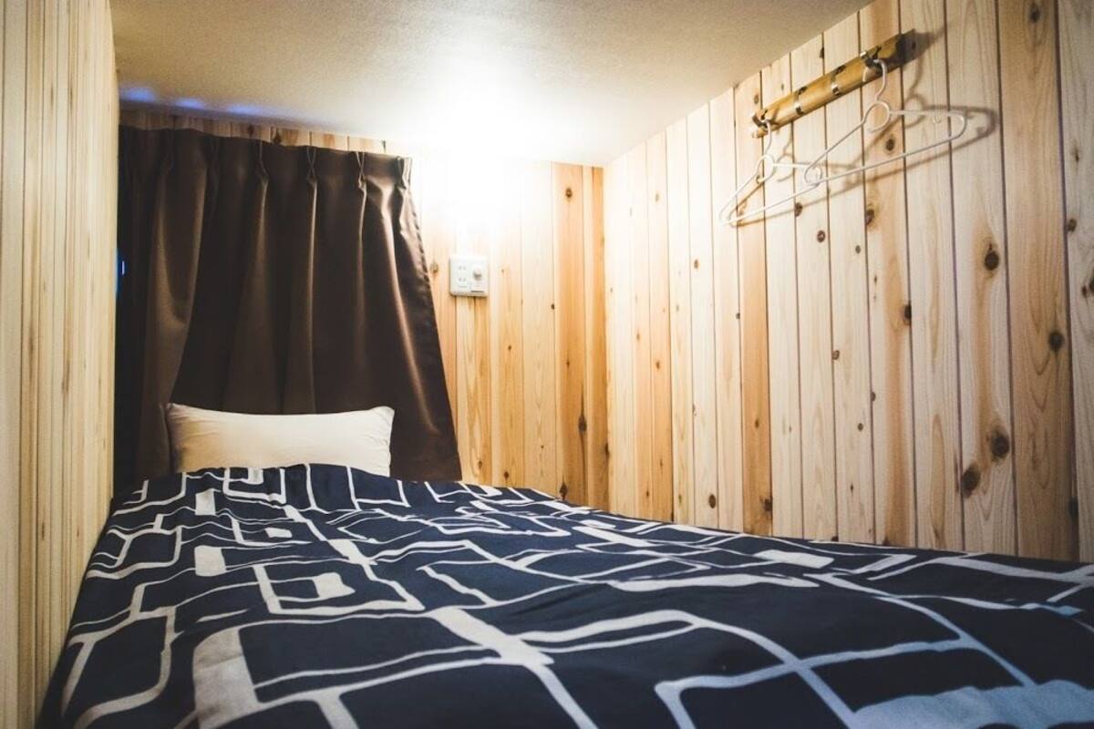Habitació amb panells de fusta, un llit, una làmpada penjant i un penjador.