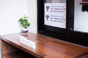 Un mostrador de recepción con un letrero que indica acceso a Wi-Fi y una planta a la izquierda.