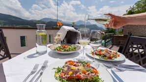 Une table dressée pour un repas, avec une vue sur la montagne, une bouteille d’eau et deux verres de vin blanc.