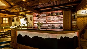 Un espace bar agrémenté de poutres en bois, un comptoir de bar orné d’un motif représentant une silhouette de montagne, et des étagères remplies de bouteilles et de verres.