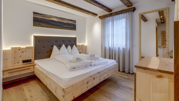 Une chambre à coucher avec un cadre en bois, un grand lit, une tête de lit, un tableau et un miroir.
