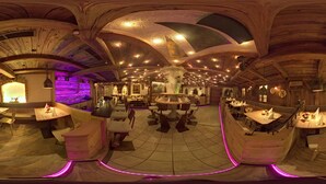 Un vaste espace de restauration circulaire, doté de tables et de chaises en bois, d’un bar central et d’un plafond voûté élevé avec des poutres apparentes.