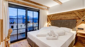 Une chambre d’hôtel moderne dotée d’un grand lit, de poutres apparentes en bois au plafond, d’une vue sur les montagnes et d’une porte-fenêtre coulissante donnant sur le balcon.