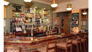 A bar area with a brick counter, multiple liquor bottles, and bar stools. - The Crown Hotel (Hailsham)