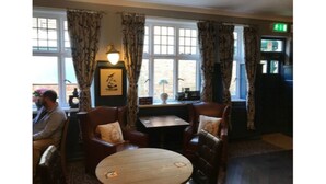 A room with two wooden tables and four leather chairs, a small table with a potted plant, and a window with curtains. - The Crown Hotel (Hailsham)