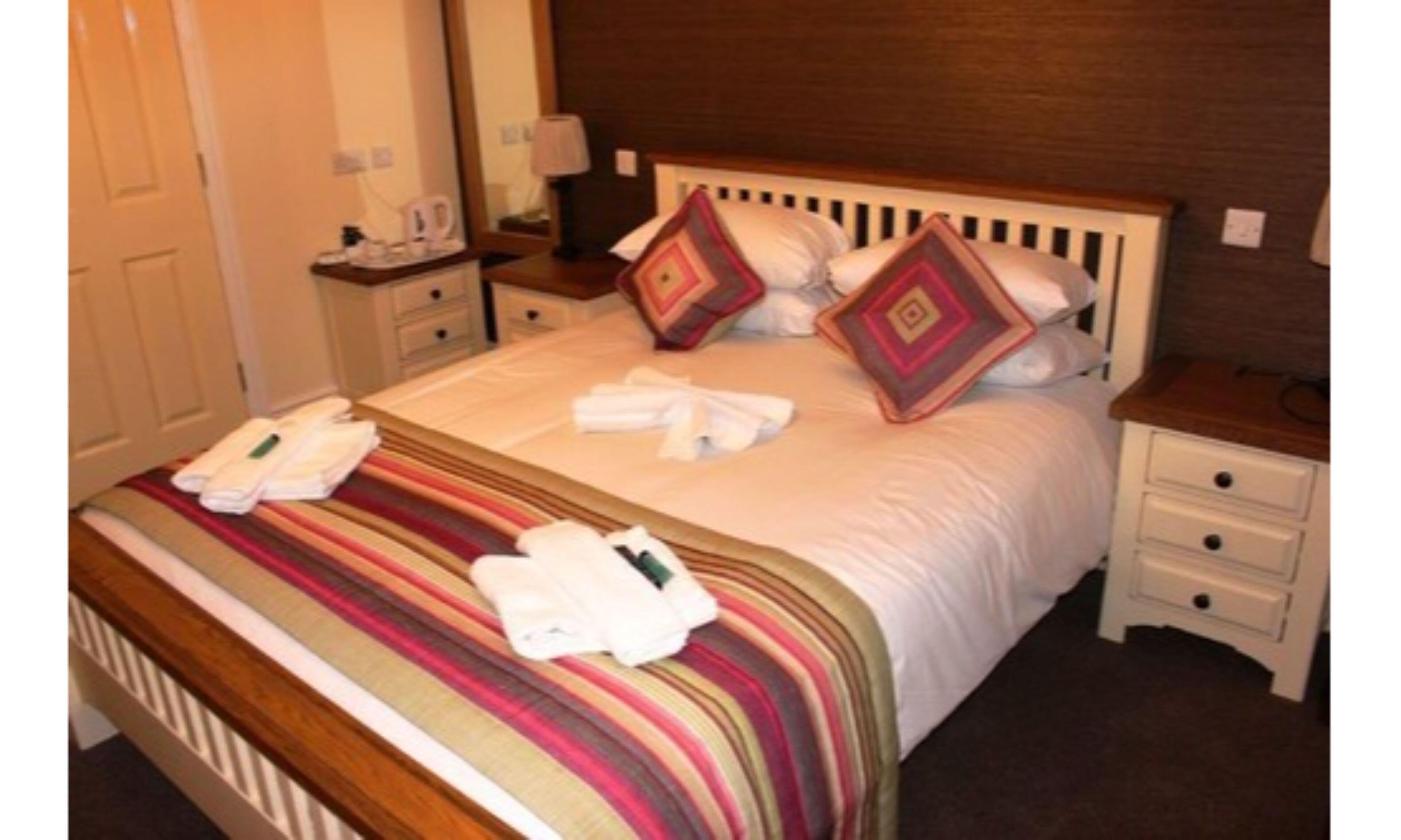 A neatly made bed with striped bedding, two pillows, and a set of towels on the side.