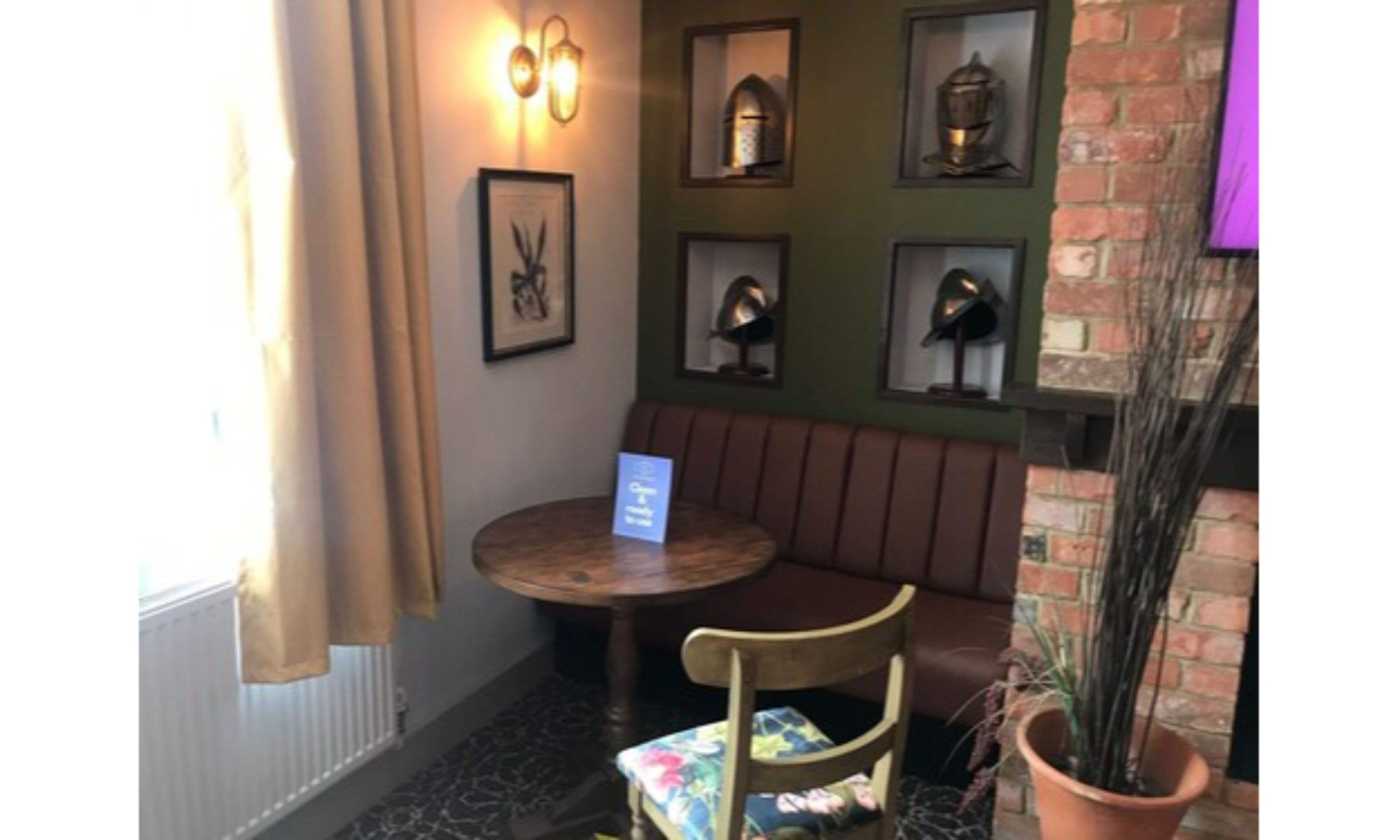 A corner seating area with a round table and a cushioned chair, a framed picture on the wall, and a potted plant.