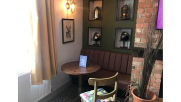 A corner seating area with a round table and a cushioned chair, a framed picture on the wall, and a potted plant.