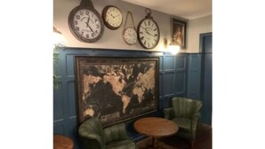 A room with two green armchairs, a small wooden table, and three wall clocks. - The Crown Hotel (Hailsham)