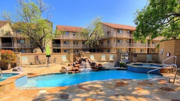 A pool area with a waterfall feature, lounge chairs, and a stone-tiled deck.
