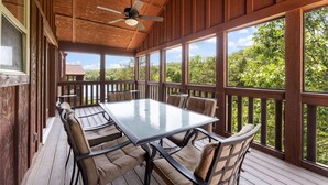 Una terrazza coperta all'aperto con tavolo e sedie dotati di piano in vetro, ringhiere in legno e una ventola a soffitto.