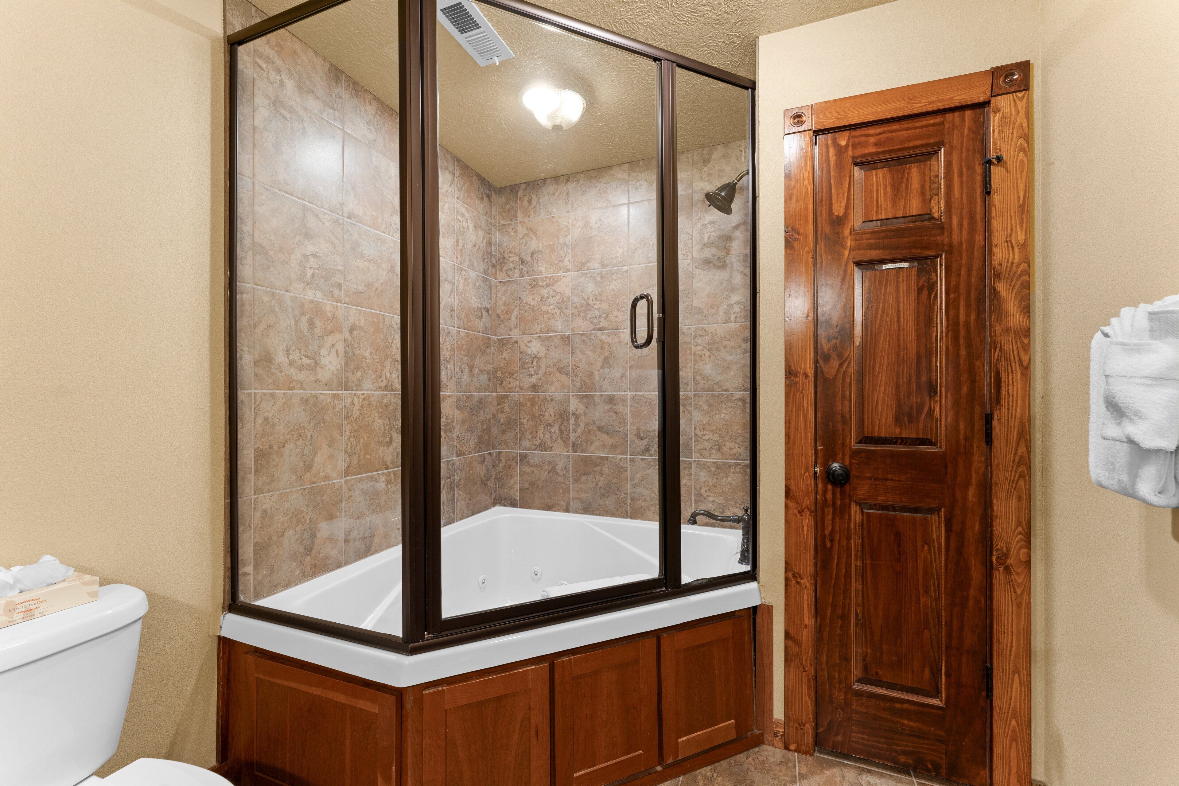 A bathroom with a glass-enclosed shower, a wooden door, and a white bathtub.