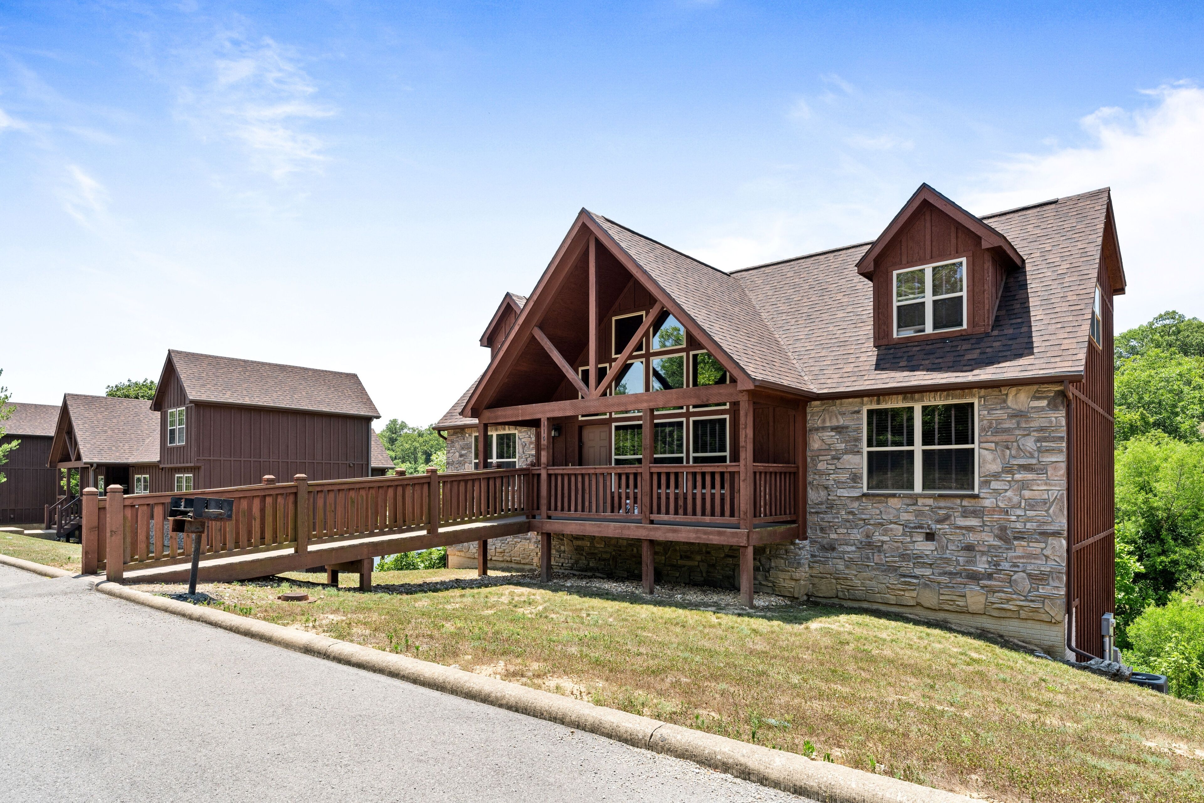 A two-story house with a stone facade, a wooden deck, and a covered walkway.