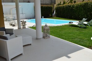 Zona junto a la piscina con sillones de descanso, una mesita y un sofá de mimbre blanco.