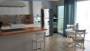 Eine moderne Küche mit weißen Schränken, einem Edelstahlkühlschrank und einer Holzarbeitsplatte. Es gibt einen Essbereich mit einem weißen Tisch und Stühlen.