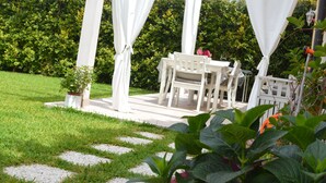 Eine weiße Pergola mit weißen Vorhängen, einem Tisch und Stühlen in einem Garten.