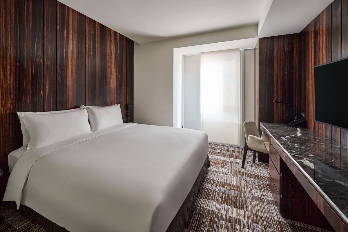 A hotel room with a large bed, a desk with a flat-screen TV, and a window with a view of the outdoors.
