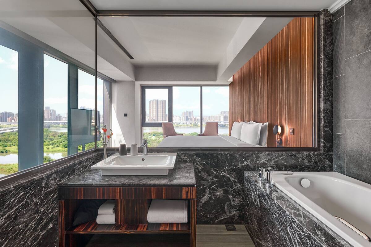 A modern bathroom with a large window, a bathtub, and a vanity with a sink.
