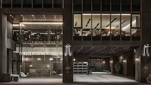 A modern hotel lobby with a reception desk, seating area, and a staircase leading to upper floors.