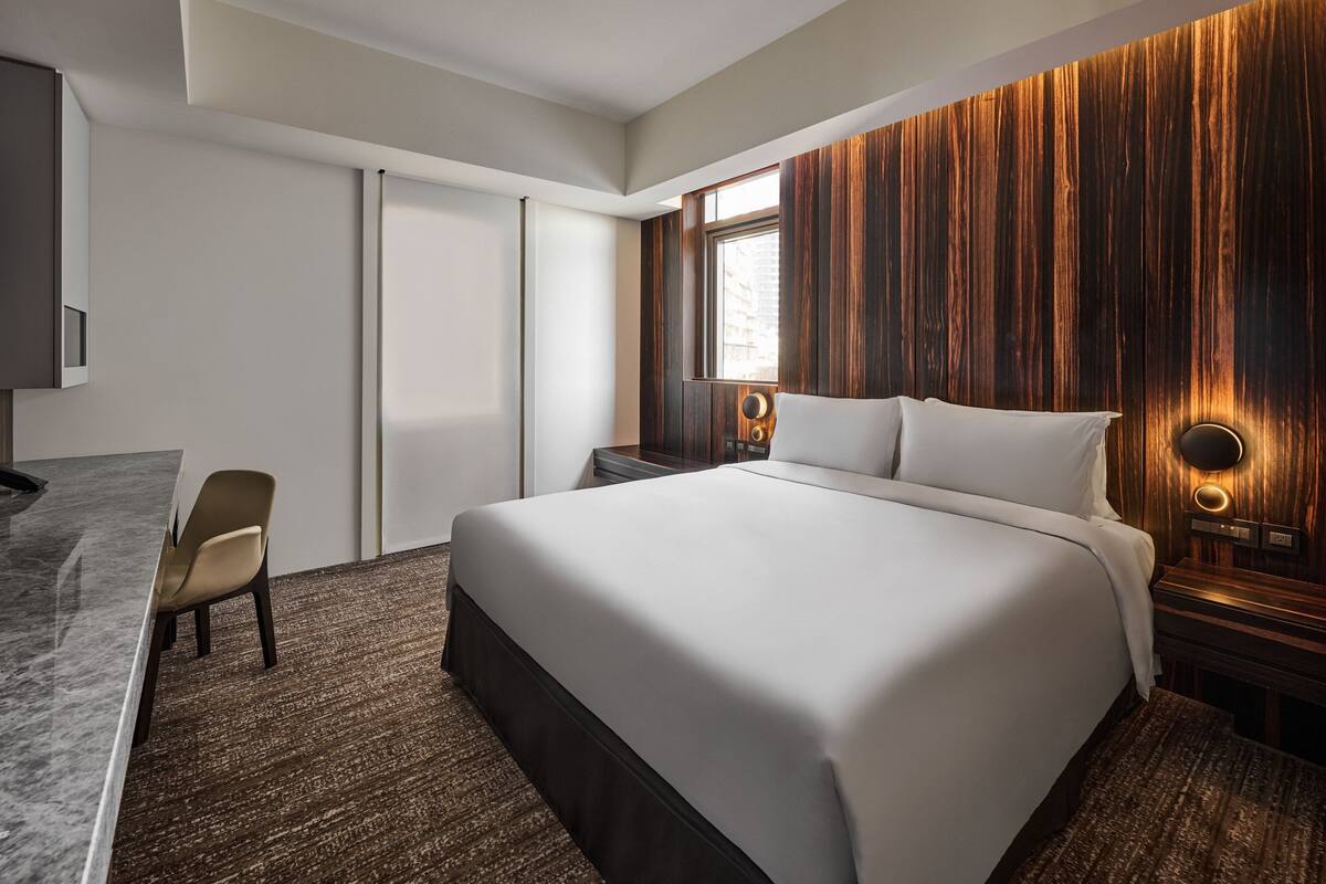 A modern hotel room with a large bed, a desk, and a chair.