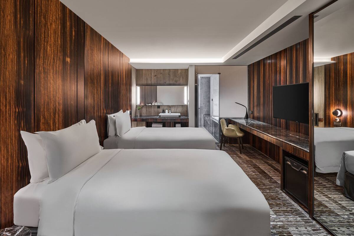 A hotel room with two beds, a desk, a TV, and a bathroom.