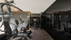 A modern gym with various exercise machines, a carpeted floor, and glass walls.