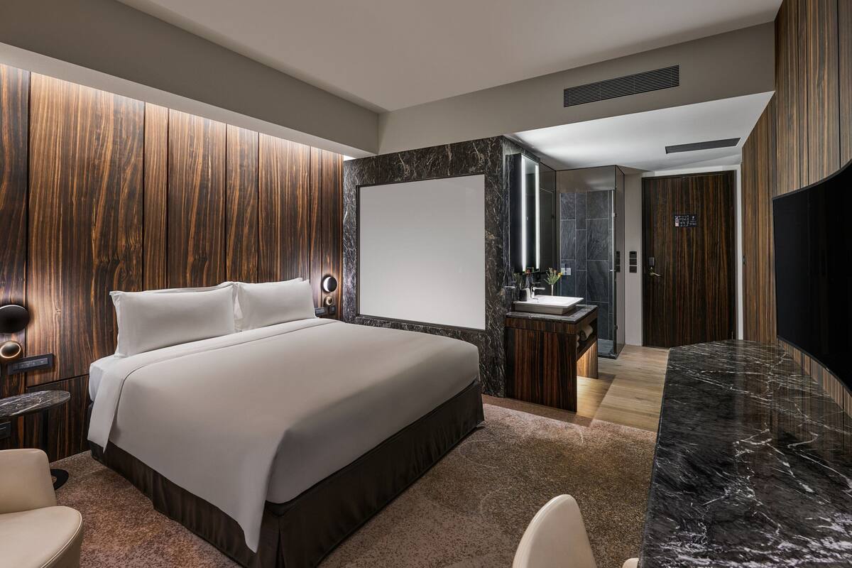 A modern hotel room with a large bed, a vanity with a mirror, a television, and a wooden accent wall.