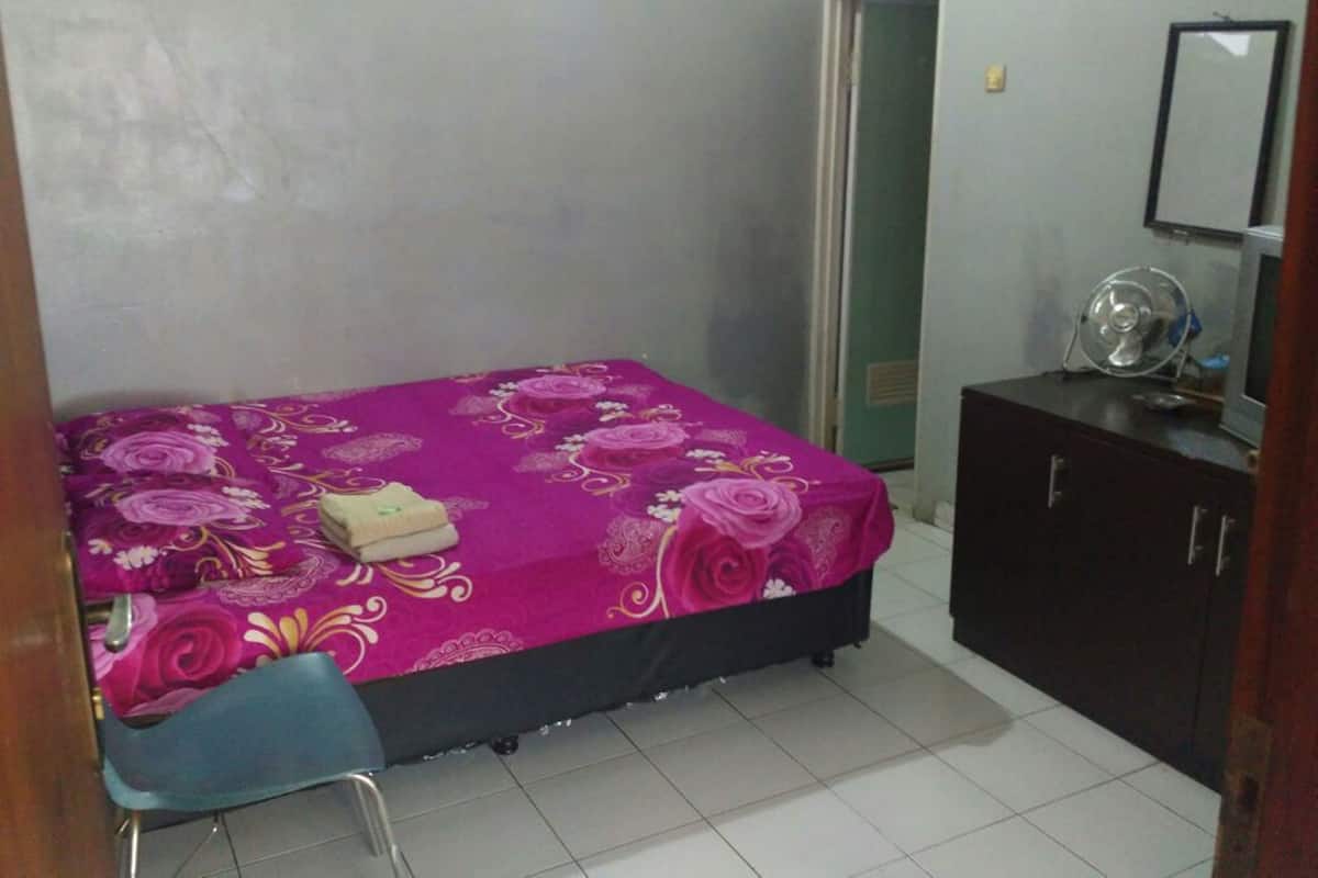 A small bedroom with a bed, a desk, a chair, a dresser, and a mirror.