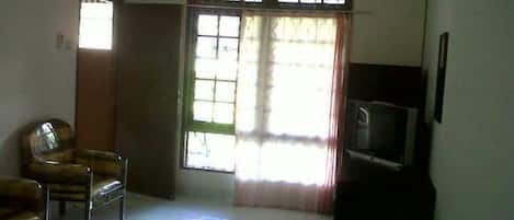 A room with a bed, a chair, a television, and a window with curtains.